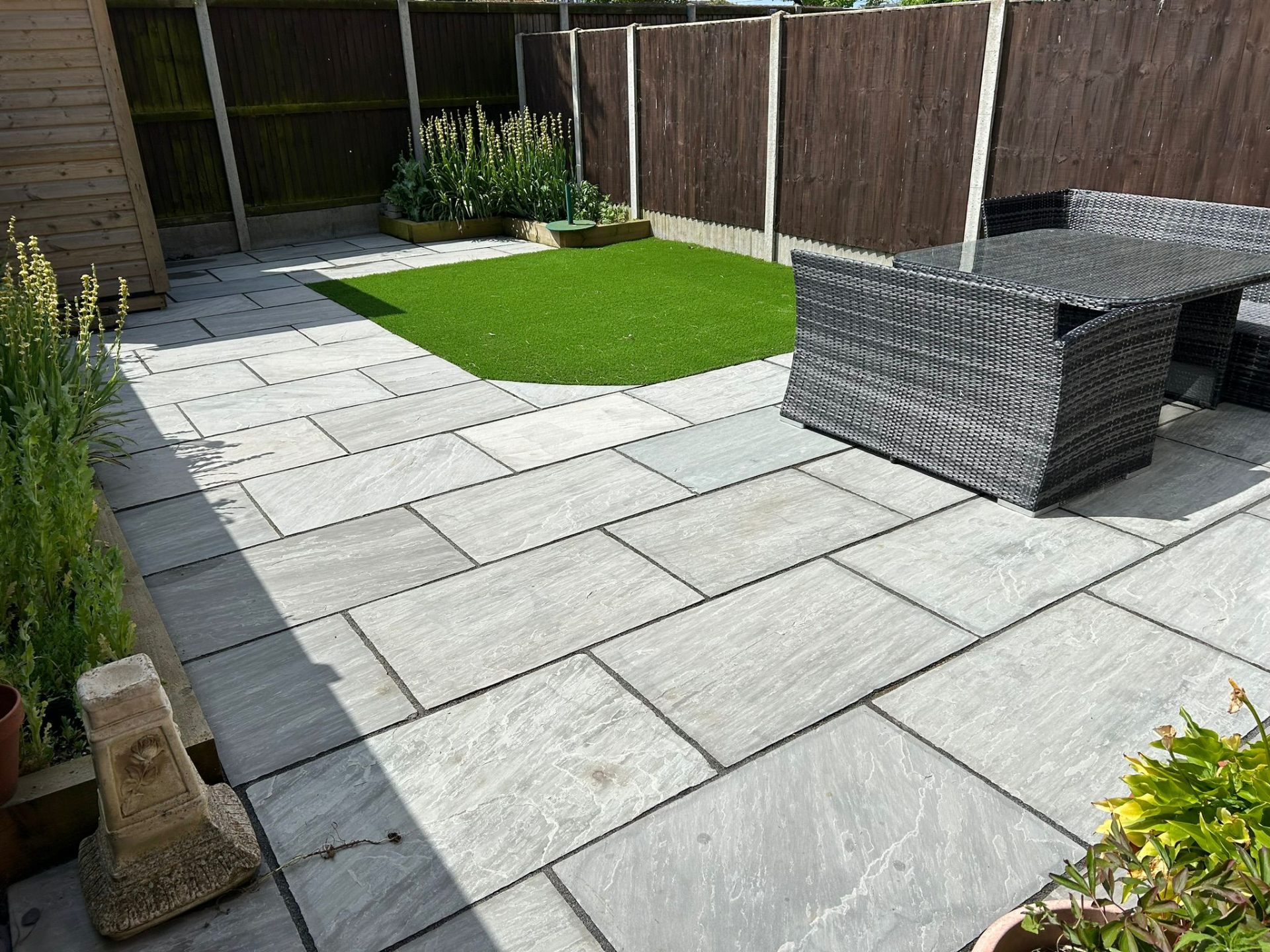Professional patio cleaning results showing clean grey stone paving with outdoor furniture and artificial grass
